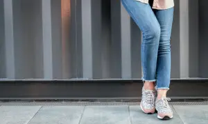 Nogawki dżinsów postrzępione na dole, modny trend. Stylowe sneakersy z błyszczącymi detalami.
