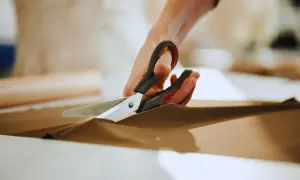 Ręce trzymają nożyce, precyzyjnie wykonując cięcie na brązowym materiale. To przykład podstawowych technik krojenia.