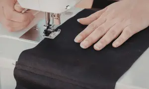 Ręce szyjące czarną tkaninę na maszynie, tworząc własną torbę DIY.
