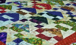 Kolorowy patchwork z geometrycznymi wzorami, wykonany techniką pikowania tkanin. Wzory przypominają góry i doliny.