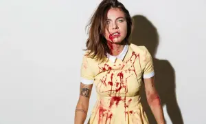 Przerażający strój na Halloween: dziewczyna w żółtej sukience z plamami krwi, z makijażem sugerującym ranę.