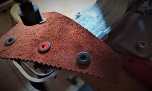 Zbliżenie na narzędzie do nabijania zatrzasków na skórzanym materiale.
