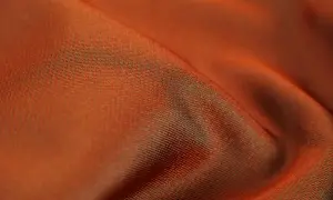 Pomarańczowy materiał acetate z subtelnym połyskiem, układający się w miękkie fałdy.
