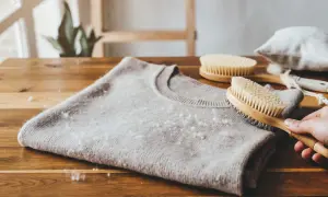 Szara, wełniana bluza z mechacącymi się kuleczkami, obok szczotki do ubrań.