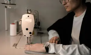 Mężczyzna w okularach pracuje przy maszynie do szycia, kontrolując siłę naciągu nici.