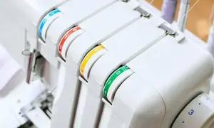 Biała maszyna ściegu obrzucającego z kolorowymi pokrętłami do regulacji naprężenia nici.