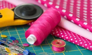 Różowe nici, szpilki, rolka do tkanin i materiały z wzorami – idealny zestaw do szycia z tkaniny **non woven**.