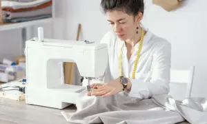 Krawcowa pracuje przy maszynie, dobierając odpowiednie rozmiary igieł do tkaniny.