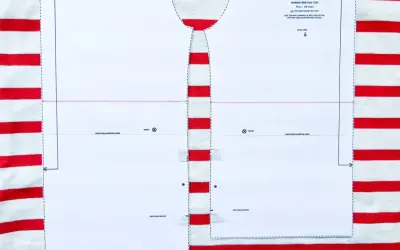 Wzór wykroju na bluzkę typu bretońskiego leży na materiale w biało-czerwone paski. Dzianina w paski idealnie pasuje do morskiego stylu.