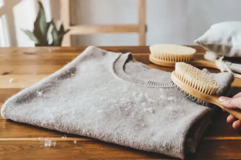 Delikatny sweter z kaszmiru z widocznymi kuleczkami, które pokazują, czy kaszmir się mechaci. Szczotka do pielęgnacji wełny w dłoni.