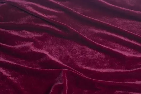 Głęboki, burgundowy materiał o miękkiej, połyskującej powierzchni, podobny do aksamitu, tworzy eleganckie fałdy.