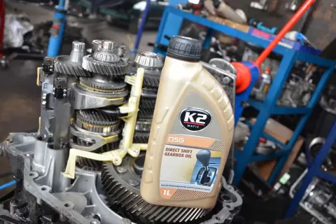 Butelka oleju do skrzyni biegów DSG na tle mechanizmu skrzyni biegów.