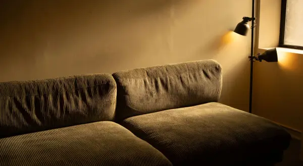 Kanapa z miękkiego sztruksu, oświetlona ciepłym światłem lampy stojącej.