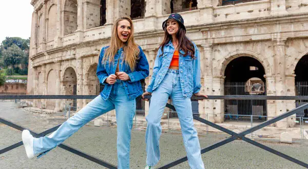 Dwie kobiety w strojach w kolorze denim pozują przed Koloseum. Jedna ma rozpuszczone włosy, druga nosi kapelusz.