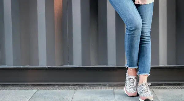Nogawki dżinsów postrzępione na dole, modny trend. Stylowe sneakersy z błyszczącymi detalami.