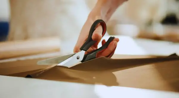 Ręce trzymają nożyce, precyzyjnie wykonując cięcie na brązowym materiale. To przykład podstawowych technik krojenia.