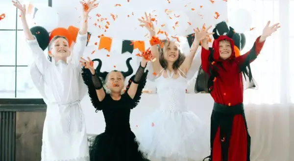 Dzieci w strojach aniołów i diabła rzucają konfetti. Inspiracja, jak zrobić strój na Halloween dla dziecka.