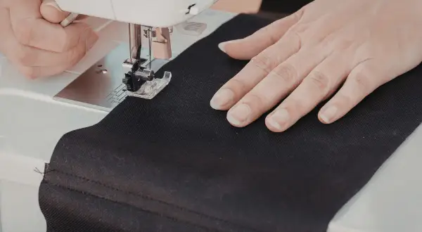 Ręce szyjące czarną tkaninę na maszynie, tworząc własną torbę DIY.