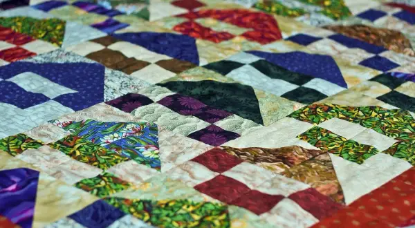 Kolorowy patchwork z geometrycznymi wzorami, wykonany techniką pikowania tkanin. Wzory przypominają góry i doliny.