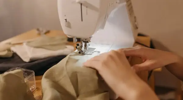 Ręce prowadzą materiał pod maszynę do szycia, by nauczyć się, jak zwęzić sukienkę w ramionach.