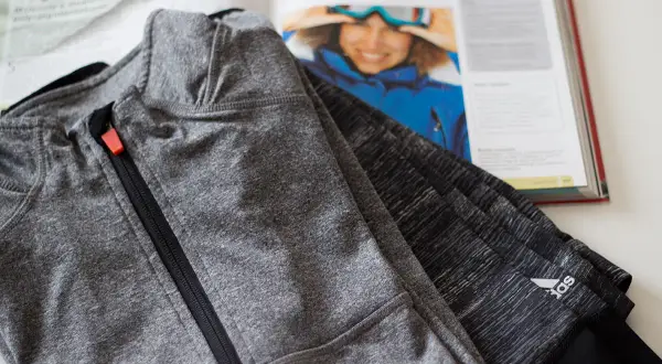 Szara bluza sportowa z zamkiem, obok otwarta książka z narciarką. Czy poliamid materiał czy oddycha?