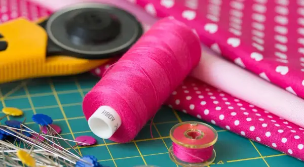 Różowe nici, szpilki, rolka do tkanin i materiały z wzorami – idealny zestaw do szycia z tkaniny **non woven**.