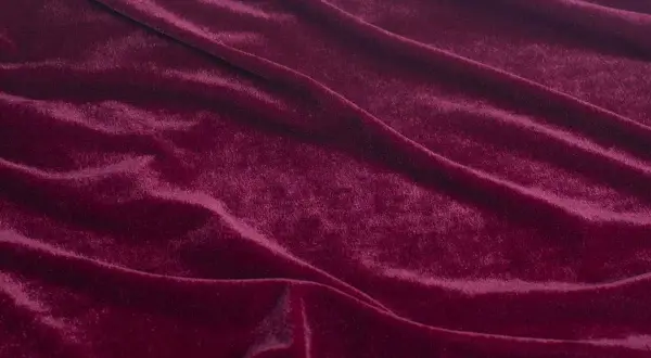 Głęboki, burgundowy materiał o miękkiej, połyskującej powierzchni, podobny do aksamitu, tworzy eleganckie fałdy.