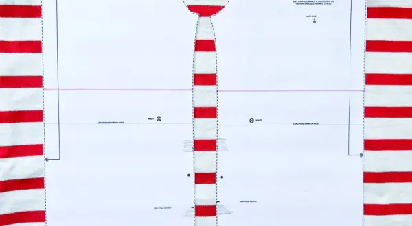 Wzór wykroju na bluzkę typu bretońskiego leży na materiale w biało-czerwone paski. Dzianina w paski idealnie pasuje do morskiego stylu.