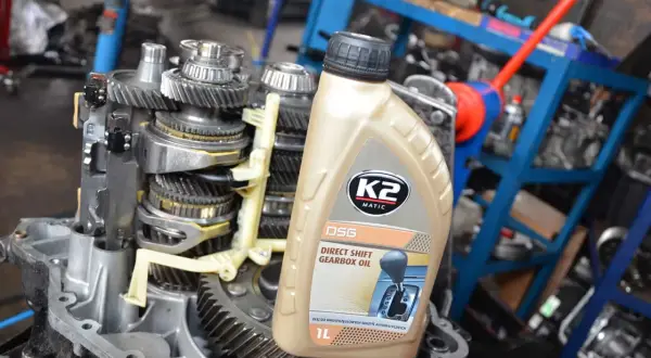 Butelka oleju do skrzyni biegów DSG na tle mechanizmu skrzyni biegów.