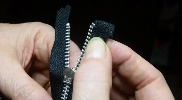 Dłonie składają czarny zamek błyskawiczny, przygotowując go do budowy.