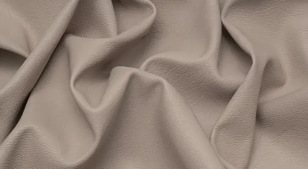 Miękka, beżowa eko skóra z delikatną fakturą, pofałdowana tworząc eleganckie draperie.