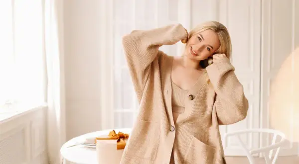 Uśmiechnięta blondynka w beżowym kardiganie i topie. Czy spandex oddycha? Jej strój wygląda na wygodny i przewiewny, idealny na ciepły dzień.
