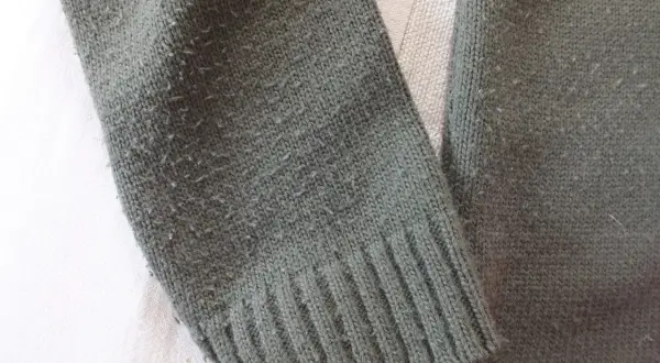 Zielony sweter z dzianiny, na którym widać, czy bawełna się kulkuje. Włókna tworzą drobne kuleczki na powierzchni materiału.