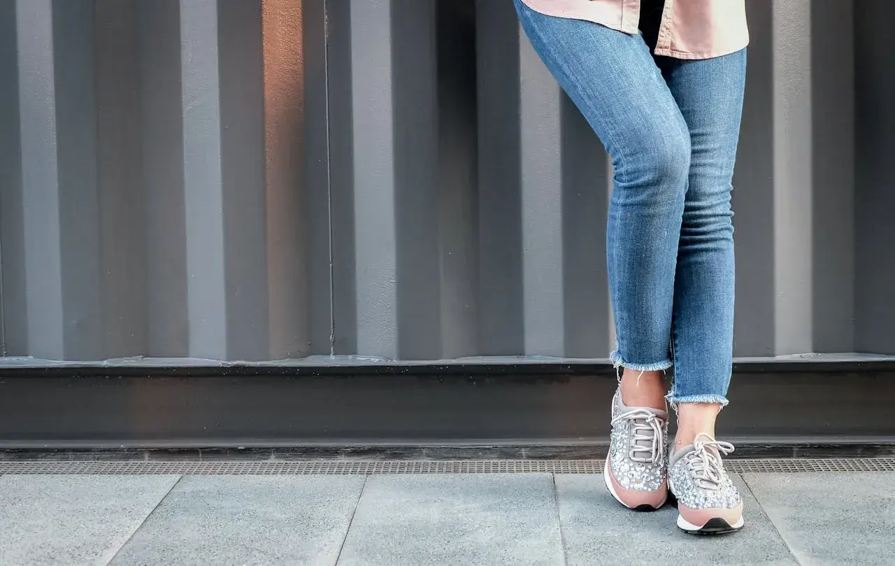 Nogawki dżinsów postrzępione na dole, modny trend. Stylowe sneakersy z błyszczącymi detalami.
