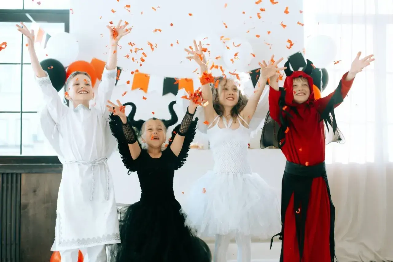 Dzieci w strojach aniołów i diabła rzucają konfetti. Inspiracja, jak zrobić strój na Halloween dla dziecka.