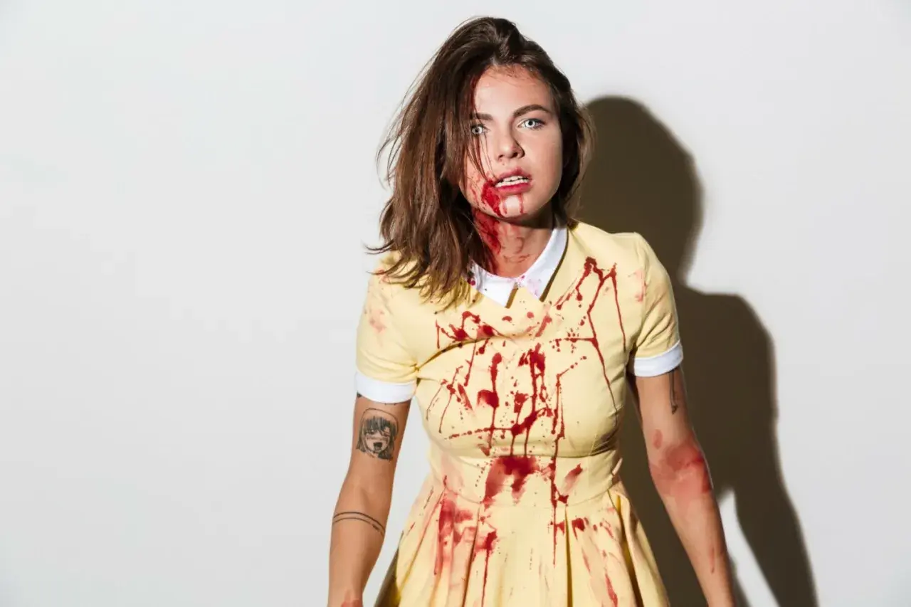 Przerażający strój na Halloween: dziewczyna w żółtej sukience z plamami krwi, z makijażem sugerującym ranę.