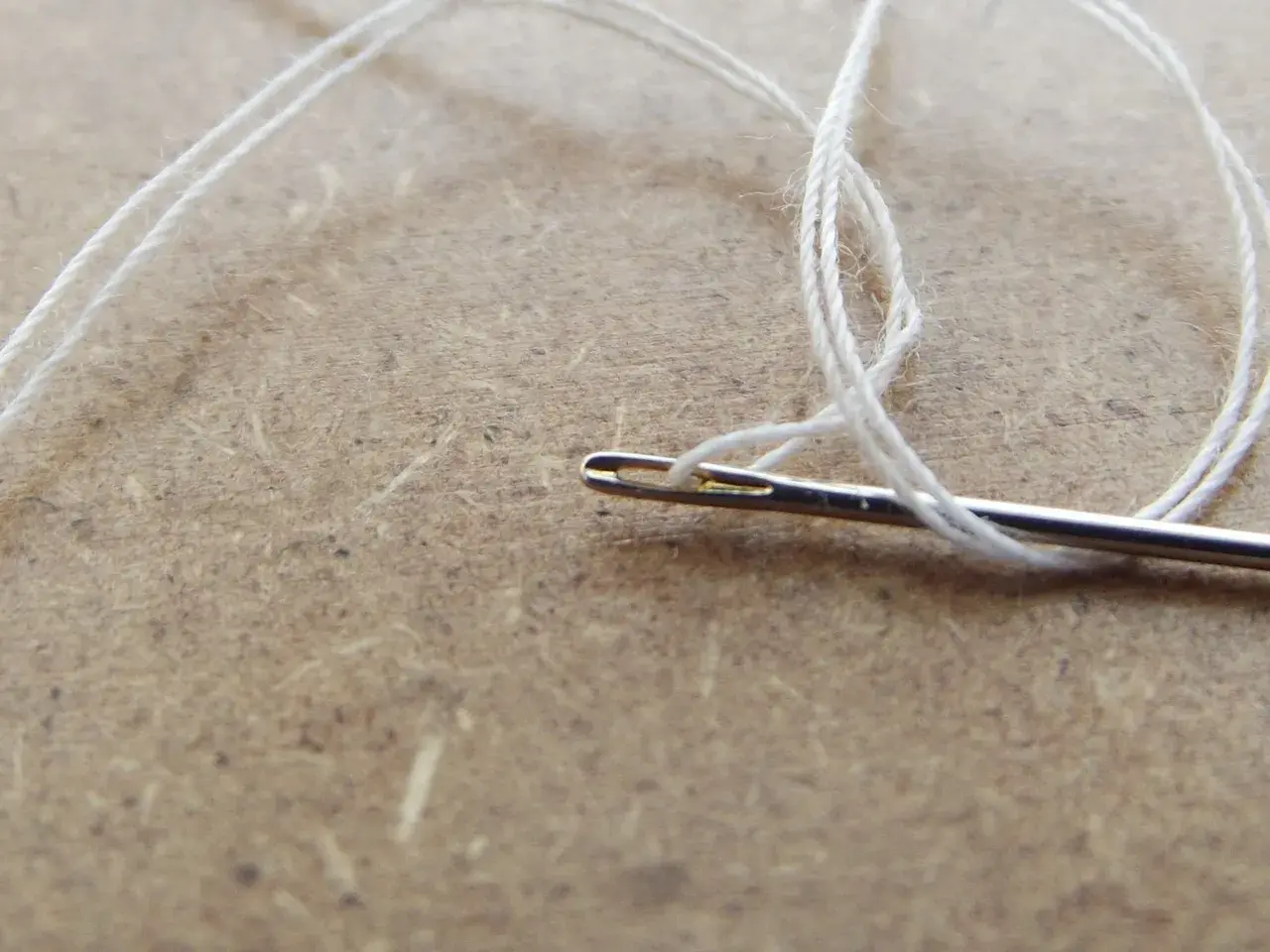 Biała nić przechodzi przez ucho igły, tworząc delikatną pętelkę. To początek szycia, może nawet naprawy ulubionej bukli.