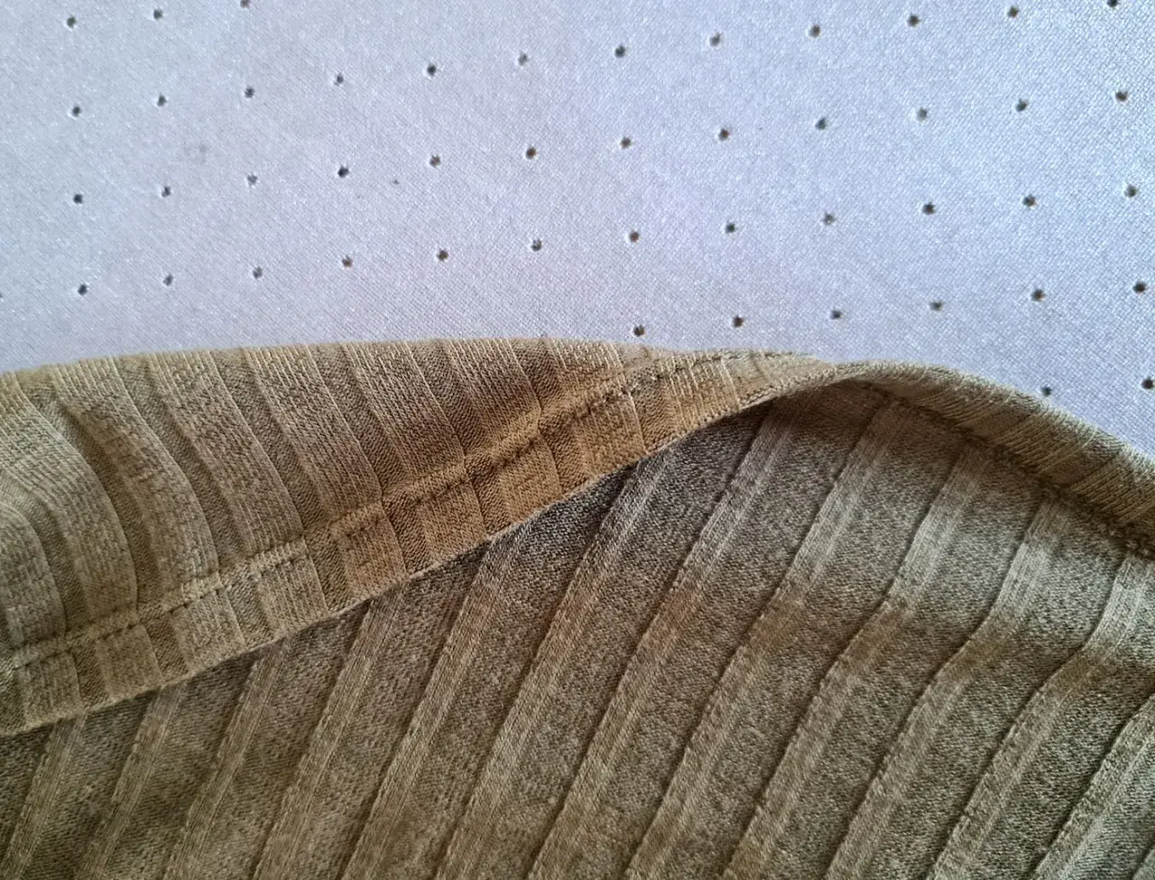 Zbliżenie na oliwkową dzianinową sukienkę z widocznym szwem i fakturą materiału.