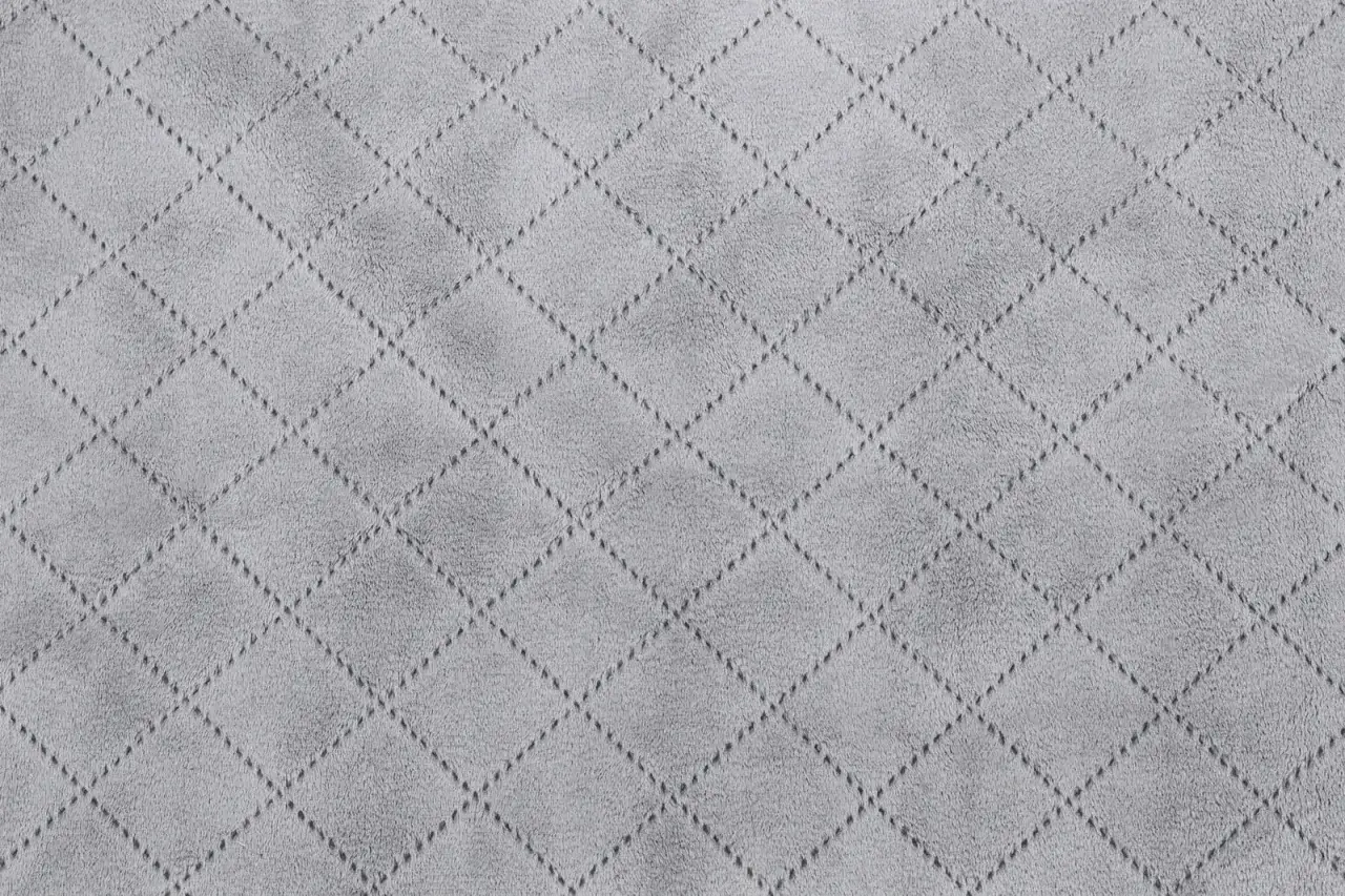 Szara tkanina z romboidalnym wzorem wykonana przez pikowanie. Delikatne przeszycia tworzą geometryczny, elegancki deseń.