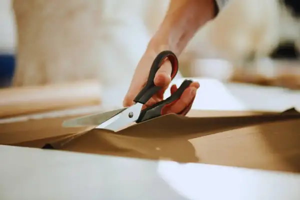 Ręce trzymają nożyce, precyzyjnie wykonując cięcie na brązowym materiale. To przykład podstawowych technik krojenia.