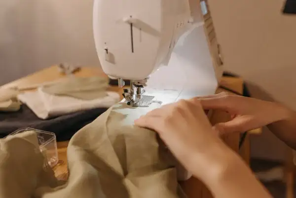 Ręce prowadzą materiał pod maszynę do szycia, by nauczyć się, jak zwęzić sukienkę w ramionach.
