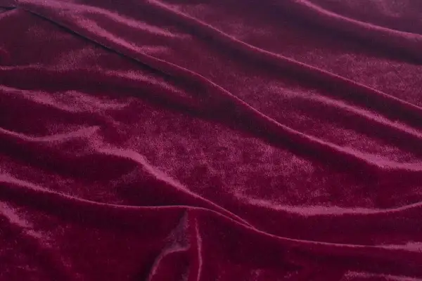Głęboki, burgundowy materiał o miękkiej, połyskującej powierzchni, podobny do aksamitu, tworzy eleganckie fałdy.