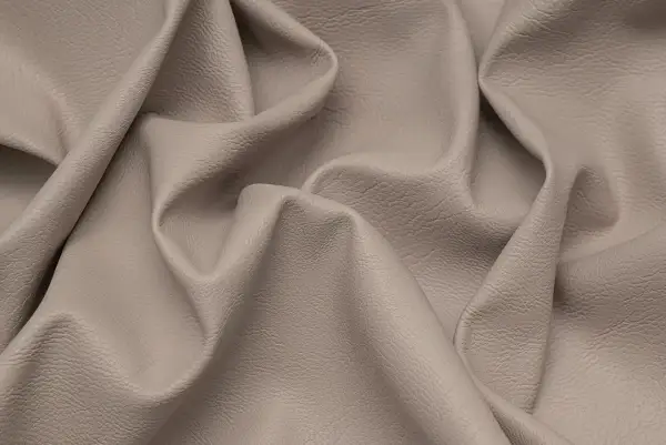 Miękka, beżowa eko skóra z delikatną fakturą, pofałdowana tworząc eleganckie draperie.